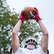 Lifestyle Image of Youth Football Player Wearing Rev 5.0 Receiver Gloves in Red Catching a Football