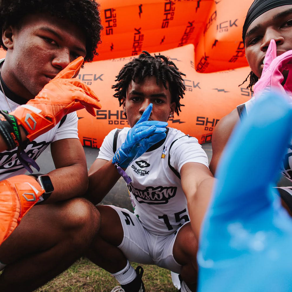 Three Youth 7v7 Football Athletes Wearing the Cutters Rev Pro 6.0 Gloves in Columbia Blue, Orange, and Pink